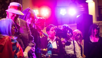 Lavalla värivalojen loisteessa cosplay asuihin pukeutuneita ihmisiä rivissä muotinäytöksessä..