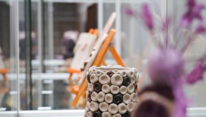 Savitöitä lasisessa vitriinissä. Keskellä ruukku ja sivussa hahmoa esittävä teos.