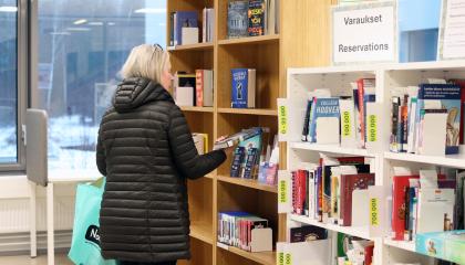 The customer is examining the back cover of a book and standing in front of the reservation shelf at Vuores Library.