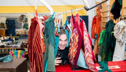 Mies kurkistaa värikkäiden vaatteiden välistä.