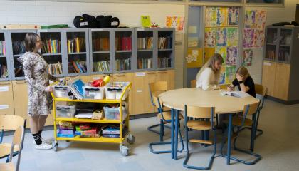 Kaksi opettajaa auttaa oppilasta läksyjen kanssa koulussa.