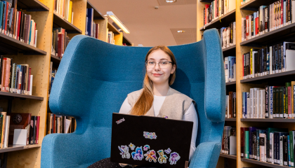 Opiskelija Daria Panova istuu nojatuolissa tietokone edessään ja takana näkyy kirjahyllyjä.