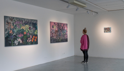 Henkilö katsoo värikkäitä ja suuria kukkatauluja taidegalleriassa.