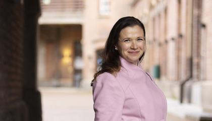 Maria Nikkilä katsoo hymyillen kameraan päällään vaaleanpunainen villakangastakki. 