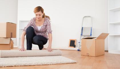 Nainen käärii mattoa rullalle ja vieressä on pahvilaatikkoja sekä tikapuut.