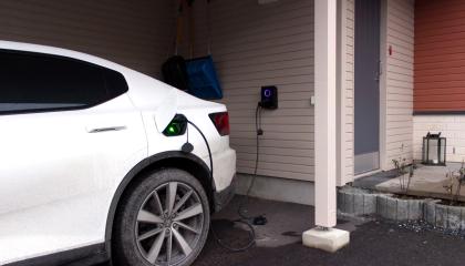 Valkoista sähköautoa ladataan autokatoksessa.