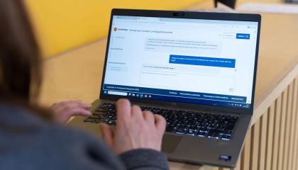 A person is studying the Entrepreneurship Advisory website on a laptop. The person is photographed from behind, with only a bit of hair, the right shoulder, and the hand visible. On the laptop screen, the webpage of the new service is displayed.