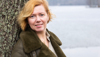 Henkilö nojaa puunrunkoon ja katsoo suoraan kameraan.