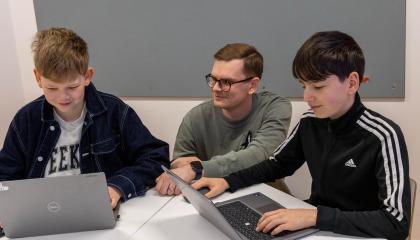 Aleksi Huttu opastaa pöydän ääressä olevaa kahta oppilasta Digimallien käytössä.