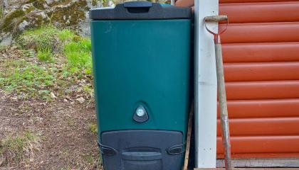 Vihreä biojätekompostori talon nurkalla.