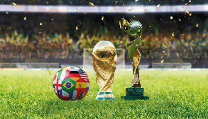 Kaksi pokaalia ja jalkapallo nurmikentällä. Taustalla katsomossa yleisöä.