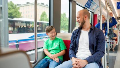 Mies ja poika istuvat bussissa, jonka ikkunasta näkyy tinen bussi.