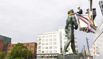 Pormestari Ilmari Nurminen seisoo nosturin lavalla turvakypärä päässään. Hän kietoo pride-väristä huivia Hämeensillan patsaan kaulaan.