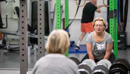 Nainen nostaa painoja kuntosalilla.