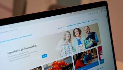 Tietokoneen ruutu, jossa on auki nettisivu. Bannerikuvassa kolme ihmistä hymyilee.