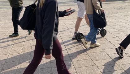 Ihmisiä kävelemässä keskustassa ja edustalla henkilö kävelee puhelin kädessä.