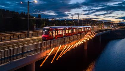Kuvassa ratikka sillalla ja valoteos kyljessä, iltahämärässä.