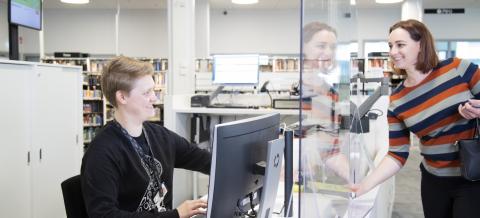 Asiakas on kirjaston tiskillä ja toisella puolella istuu työntekijä koneen äärellä.