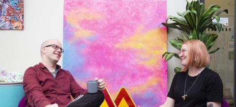 Kaksi ihmistä istuu kahvikupit kädessä vastakkain. 