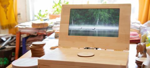 Puinen läppäri on pöydällä ja näytöllä on kuva kuikasta järvellä.