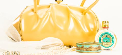 Keltaisen käsilaukun edessä on koruja ja kosmetiikkaa.