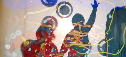 Lapset vilkuttavat värikkään kankaan takana.