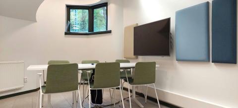 Projektihuone Jäkälän työskentelypöytä tuoleineen sekä tilan seinällä oleva näyttö.