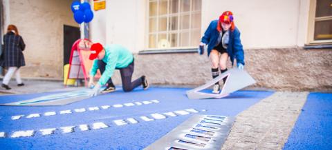 Kaksi ihmistä maalaamassa katuun sapluunakuvia.