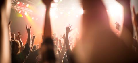 Yleisö hurraa kädet ilmassa musiikkikonsertissa.