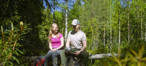 Nuori nainen ja mies levähtävät kaatuneella puulla metsässä.