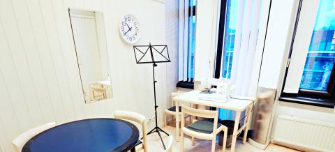 Monitoimihuone, jossa pöytä, ompelukone ja nuottiteline.