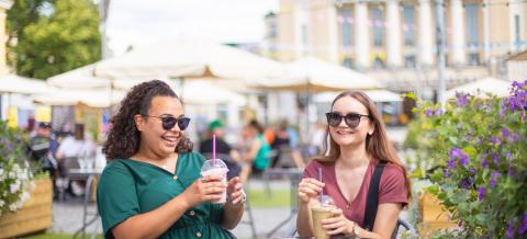 Kaksi nuorta istuu Keskustorin Kesäkeitaalla jääkahvien kanssa.
