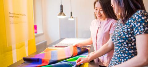 Kaksi museokävijää tutustumassa värikkäisiin kankaisiin.