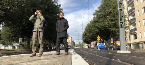 Ratikkakiskojen vieressä kaksi miestä lähdössä luontoretkelle. 