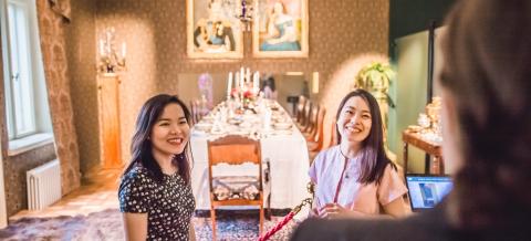 Kaksi tummahiuksista nuorta naista katsoo museonäyttelyä vanhoilla huonekaluilla sisustetussa tilassa.