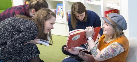 Neljä nuorta istuu ja katsoo muumikirjaa, taustalla kirjahylly.