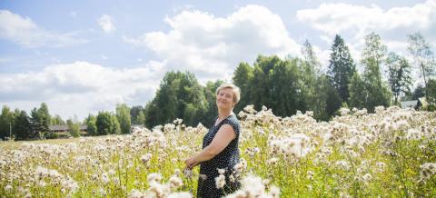 Lyhythiuksinen nainen seisoo kesällä keskellä kukkivaa Annalan peltoa.