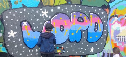 Graffiti seinä, jonka edessä kaksi lasta maalaamassa.