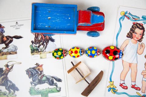 Esillä leluja, puuauto, kaarnavene, paperinukkeja.