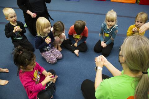 Lapset istuvat piirissä ja liikuntaohjaaja pitää heille leikkiä.