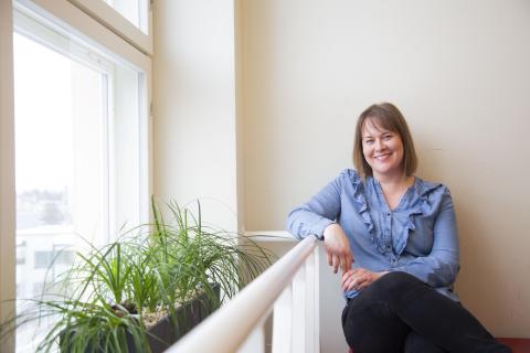 Nainen nojaa kaiteeseen ja katsoo kameraan.