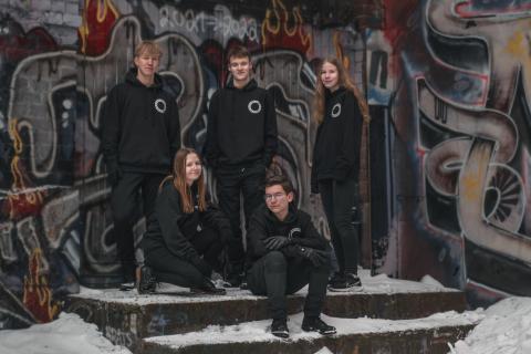 Viisi opiskelijaa graffititeoksen edessä.