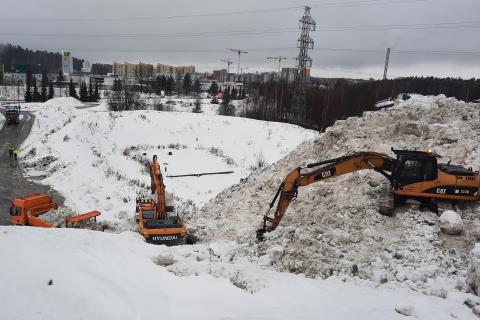 Työkoneet siirtävät lumikasoja lumenvastaanottopaikalla.
