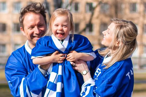 Smiling parents lift their child into the air.