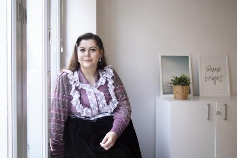 Nainen nojaa ikkunaan ja katsoo kameraan.