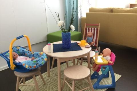 Pieniä nukkevauvoja istuu pöydän ympärillä ruokailemassa.