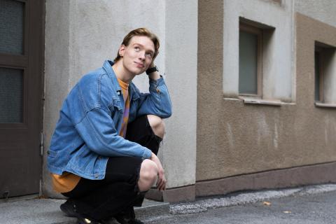 Oliver Priimägi istuu kyykyssä kadun reunassa ja katselee hymyillen ylöspäin.