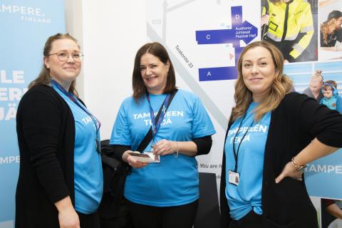 Kolme naista katsomassa kameraan. Päällä siniset t-paidat.