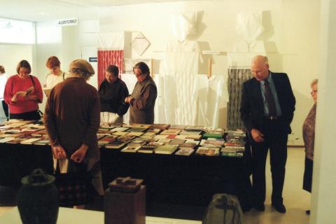 Henkilöt seisovat näyttelypöydän ääressä. Pöydällä on kädentaitotöitä.