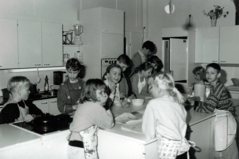 Lapset kokkaavat opetuskeittiössä. Taustalla on opettaja.